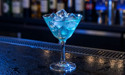 Premium-Cocktailglas mit blauem Neon-Licht und Eisw&uuml;rfeln auf dunkler Bartheke bei Casea Weekly Reload